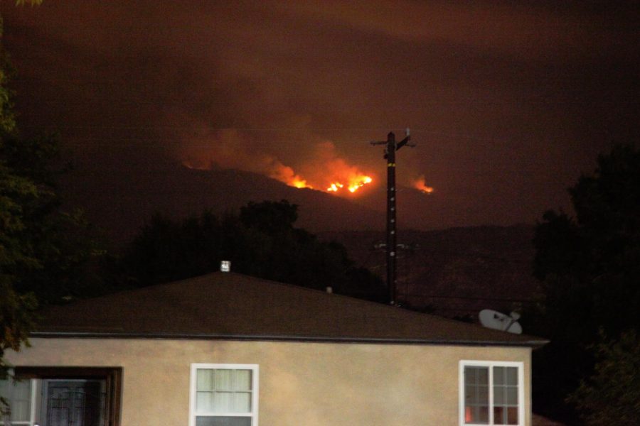 The bobcat fire rages behind a home in the hills above Monrovia, California on Sept. 9, 2020. Ashes can be see floating down and coating cars in a fine layer of grey dust. Smoke fills the air and can be seen in a dull gray haze beneath street lights. Photo credit: Abraham Navarro/SAC.Media
