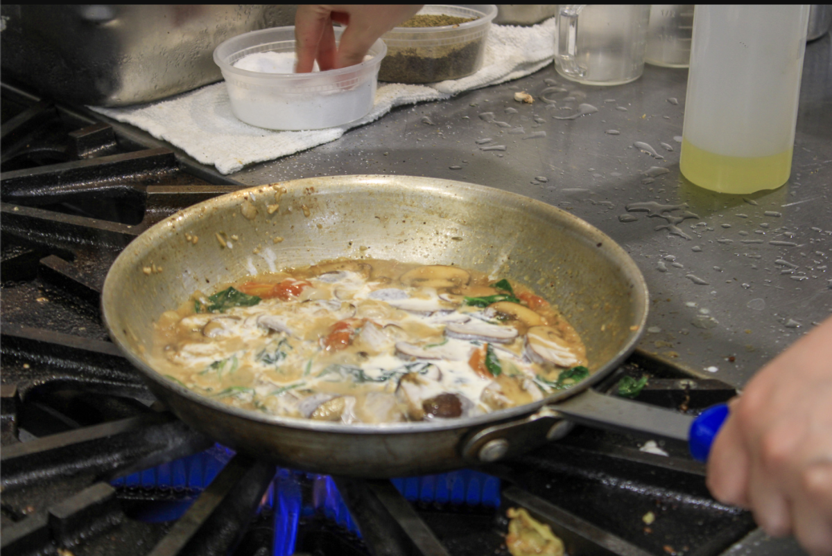 Student cook using a saucepan to make the Creamy Pasta Campanelle.