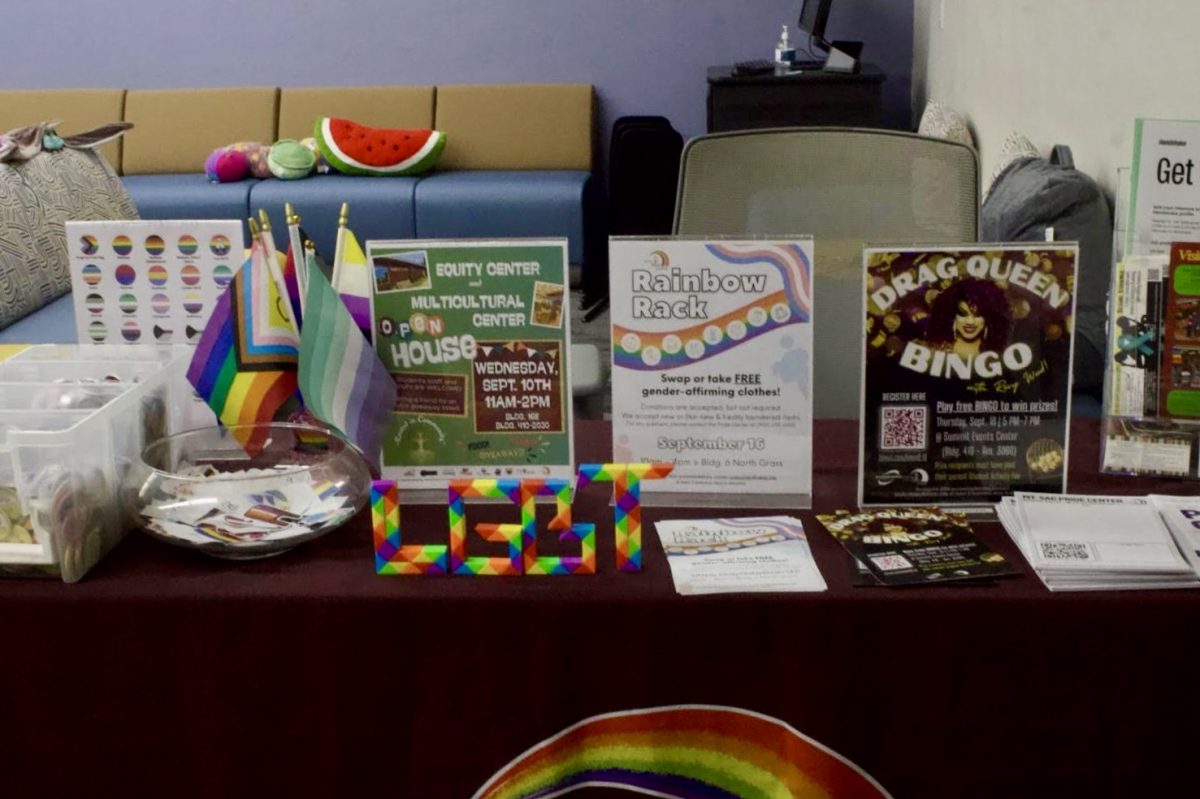 A colorful display at the Pride Center features rainbow flags, pride-themed pins, and flyers promoting events.