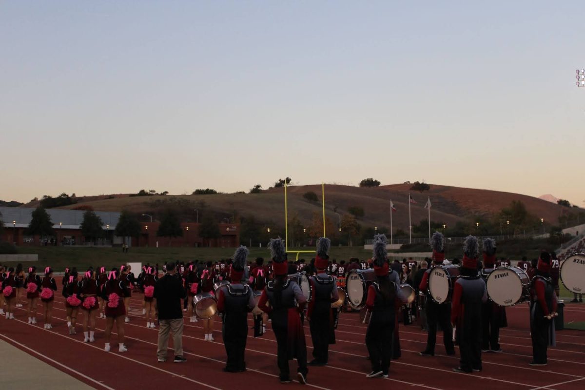 The band, cheer, dance, and color guard are facing the American flag for the "Star Spangled Banner".